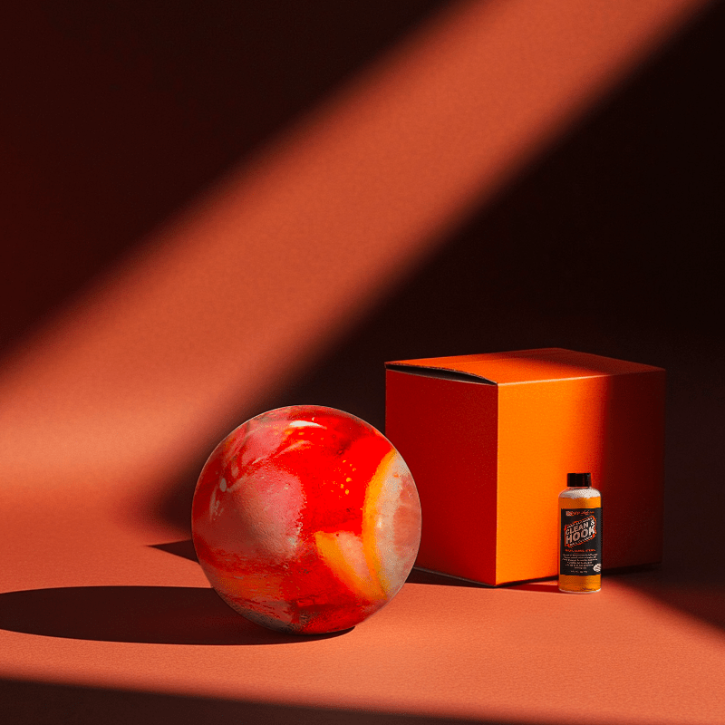 Hands holding a red orb with intricate, patterned artwork depicting a figure with sunglasses.