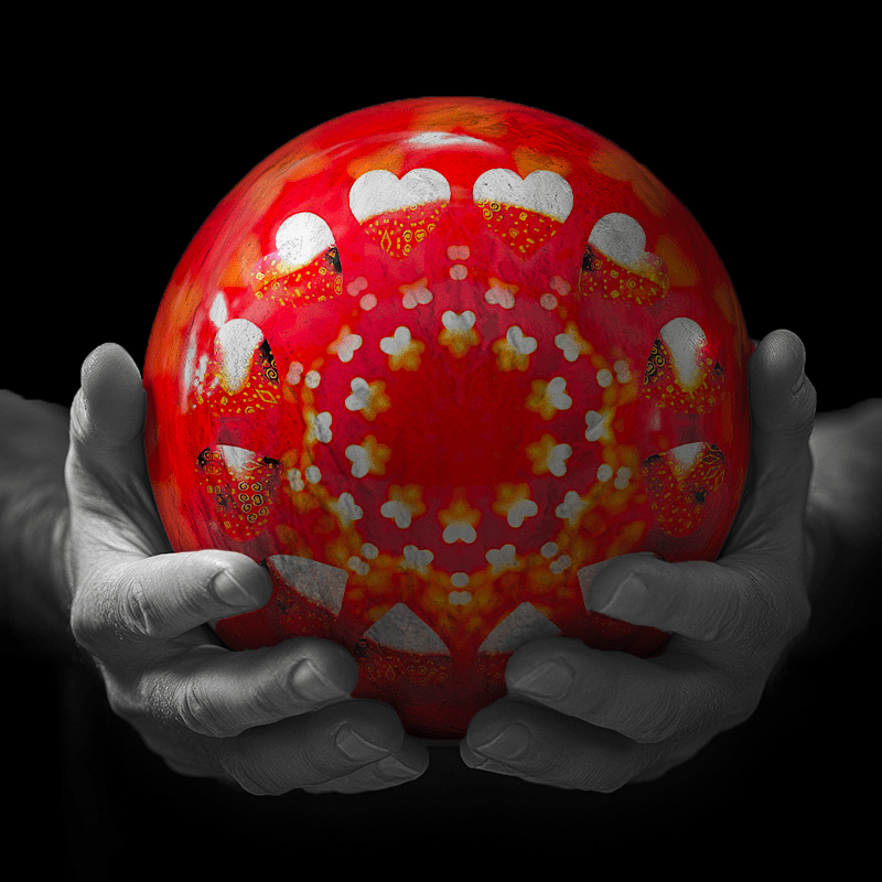 Hands holding a red sphere featuring a floral-patterned figure.